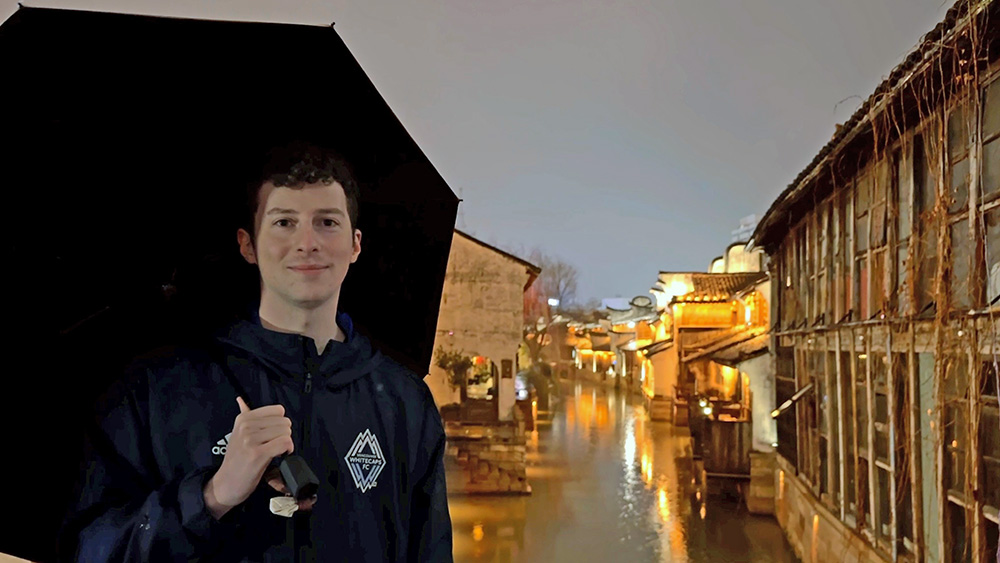 Aidan holding an umbrella with a canal scene behind him