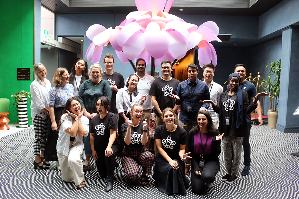A group of 17 Leadership Network members and two staff posing for a photo in front of a sculpture of a pink flower