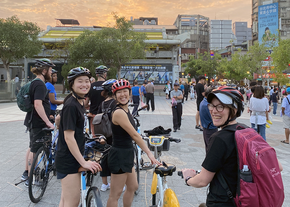 Three Leadership Network members smiling for a photo while holding bikes in an open plaza