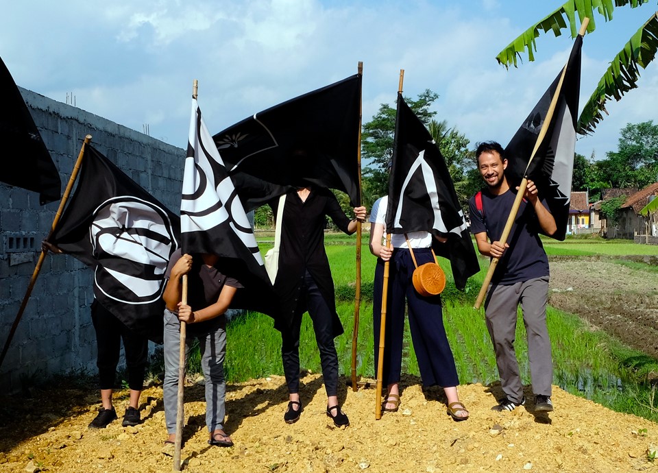 Four people standing on a mound of dirt holding black flags