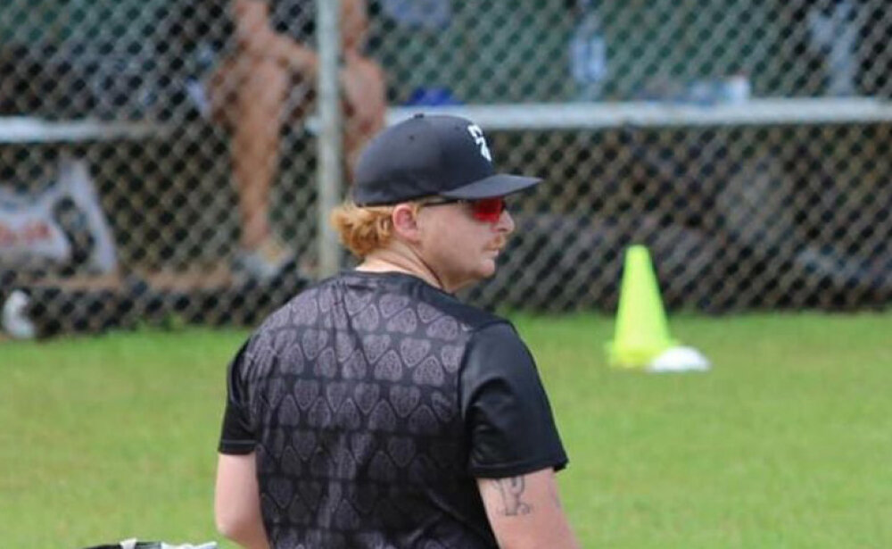 Connar- standing in a baseball field wearing a black baseball hat and suynglasses