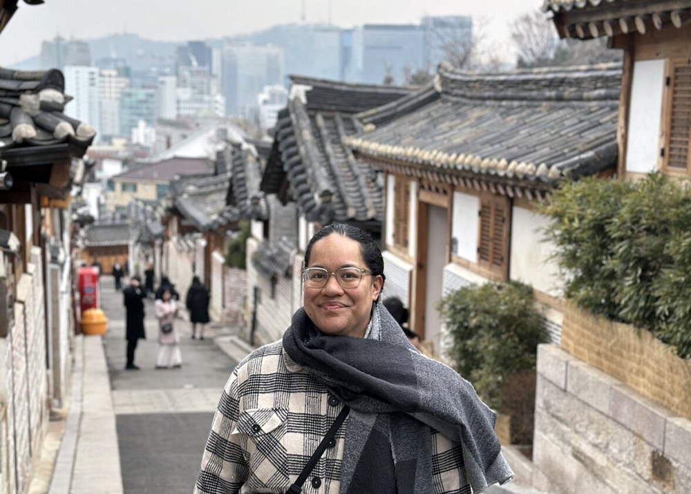Fine standing in a street of traditional Korean buildings with a panorama of Seoul behind her