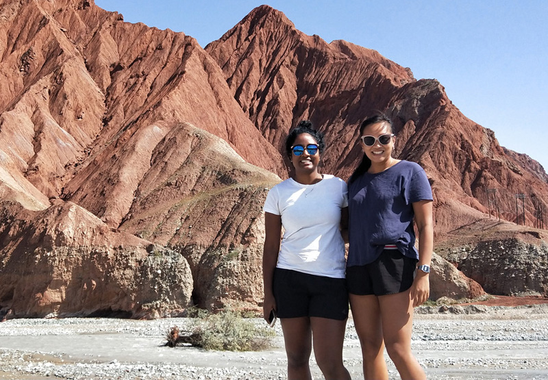 dhaxna standing with a friend in front of a red -clay mountain