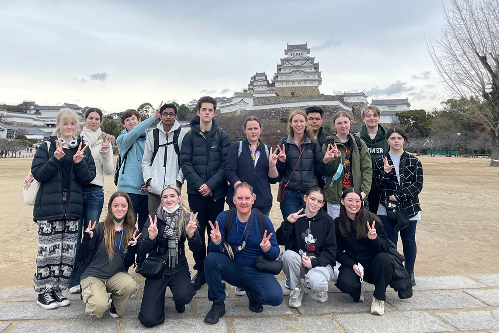 The students posing for a photo with a large traditional Japanese building in the background