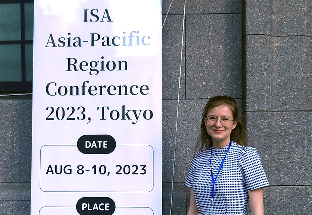 Kina Kutz staning beside a banner for the ISA Asia-Pacific conference