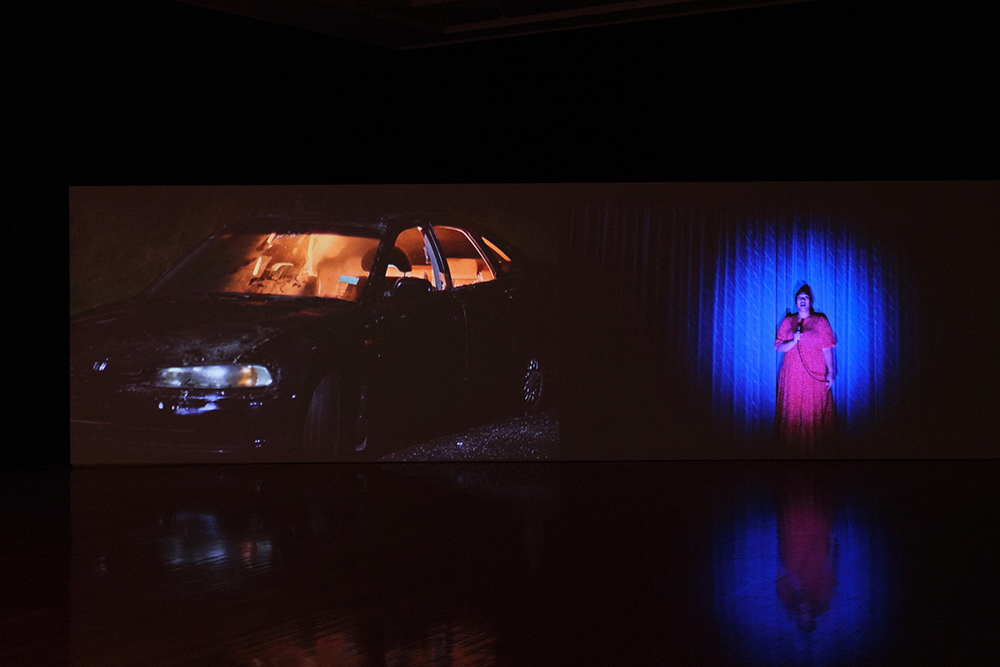 A car projected on a screen and a woman singing