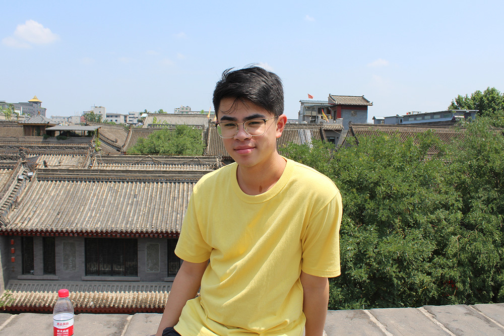Kevin sitting on a wall with traditional Chinese buildings behind him