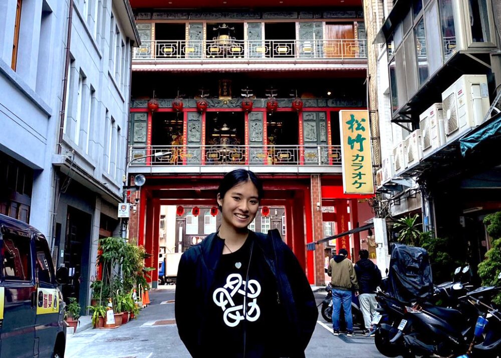 sarah standing in front of a traditional-chinese-looking building wearing an Asia New Zealand Foundation website