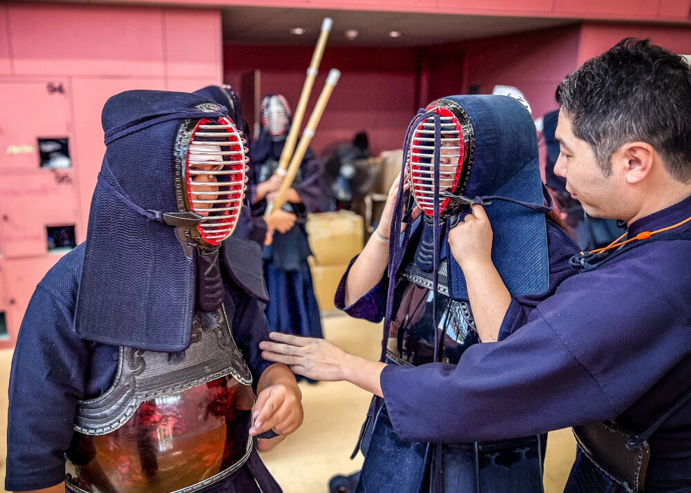Two of the team members in kendo protective gear listening to an instructor