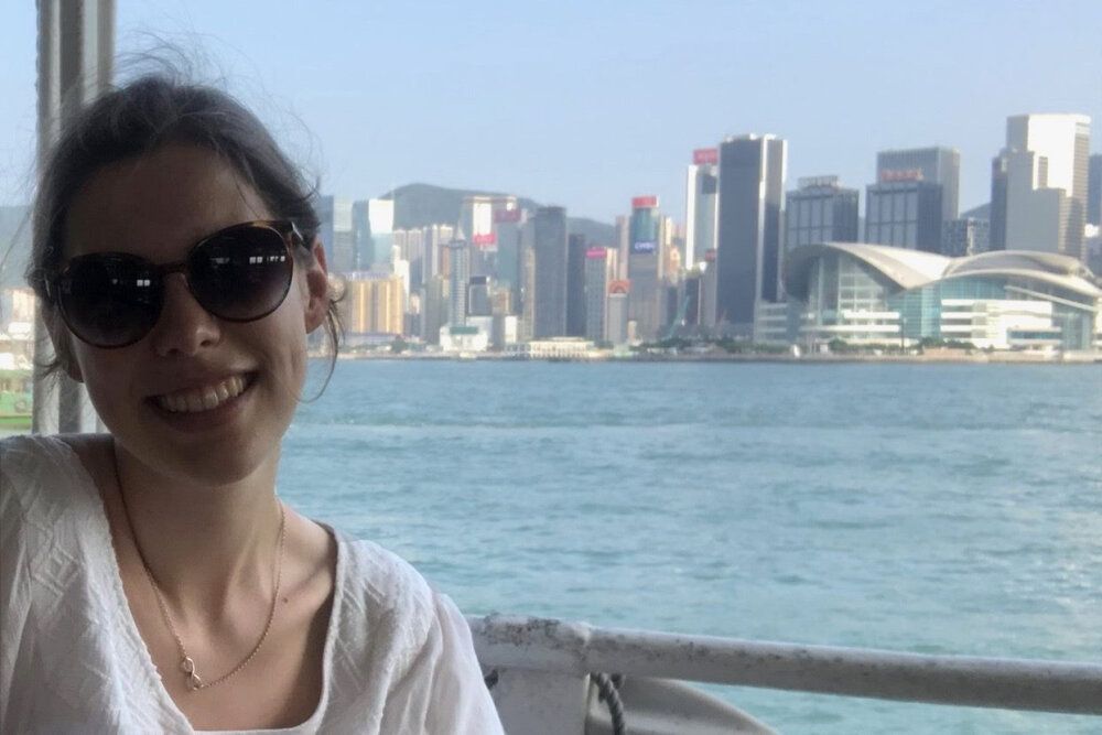 Lucy sitting on a boat with the Hong Kong skyline behind her