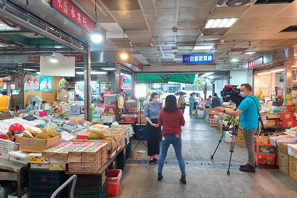 Cushla Norman being filmed interviewing a woman in a fruit and vegetable market 