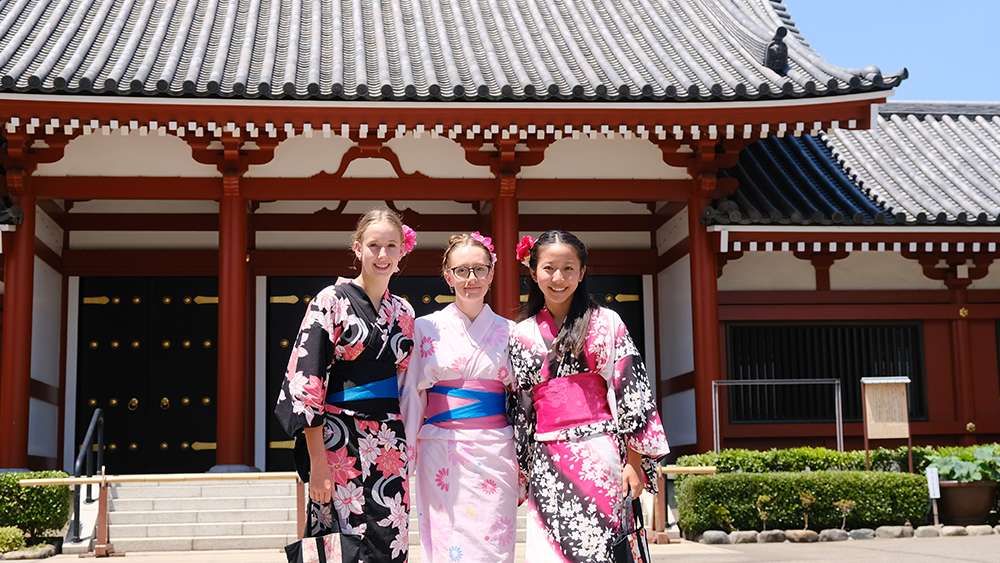 Three of the synchronised swimmers wearing kimono in front of a shrine
