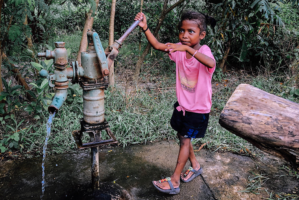 A boy using a hand pump to pump well water