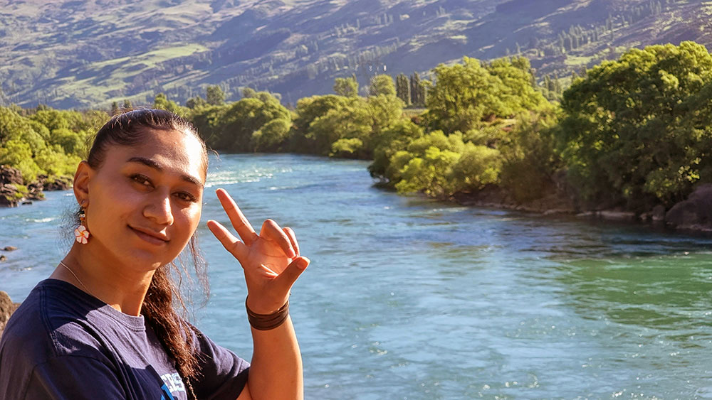 Seraphine giving the peace sign with hills and a wide river behind her