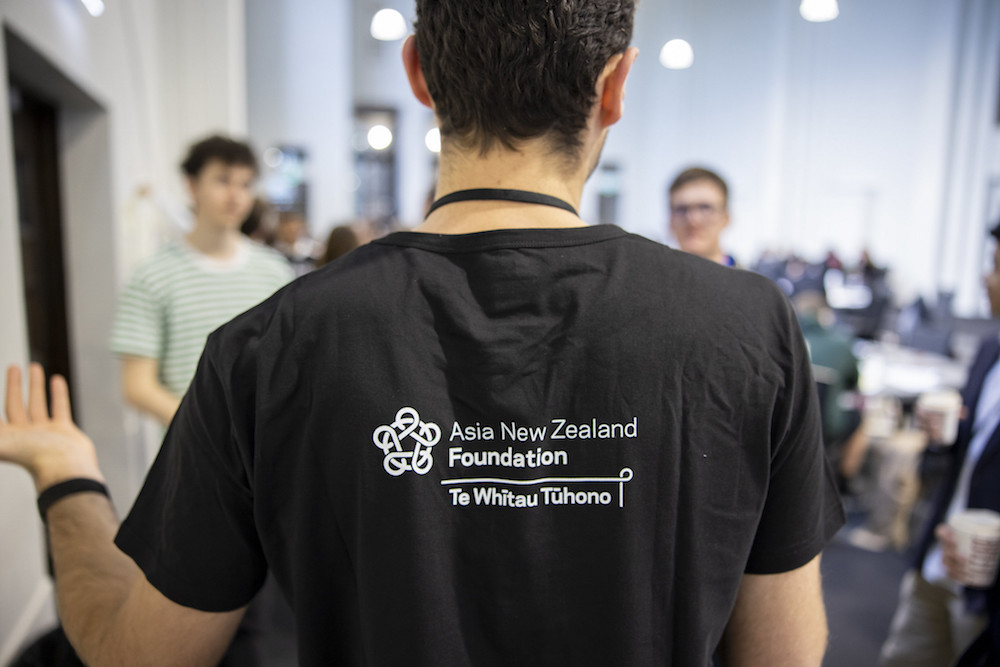 A man wearing a Asia New Zealand Foundation t-shirt talking to a group of students
