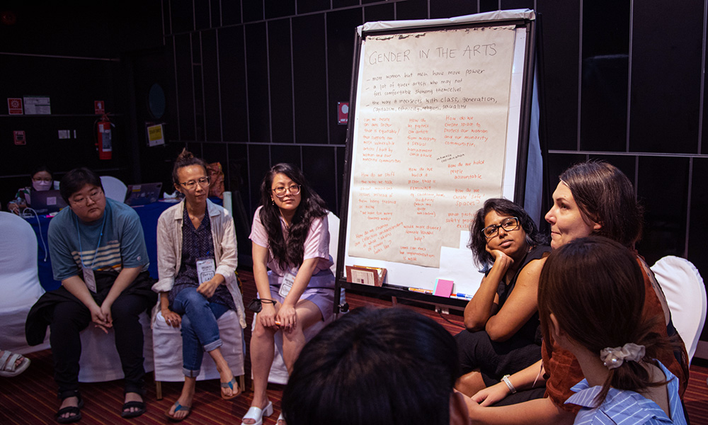 a group of people sitting on chairs in a circle talking with a giant notepad with notes on it beside them
