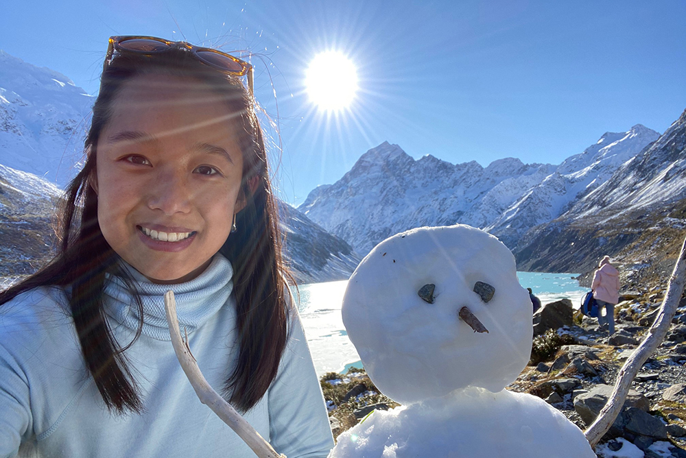 Alice standing next to a snowman in a mountainous area
