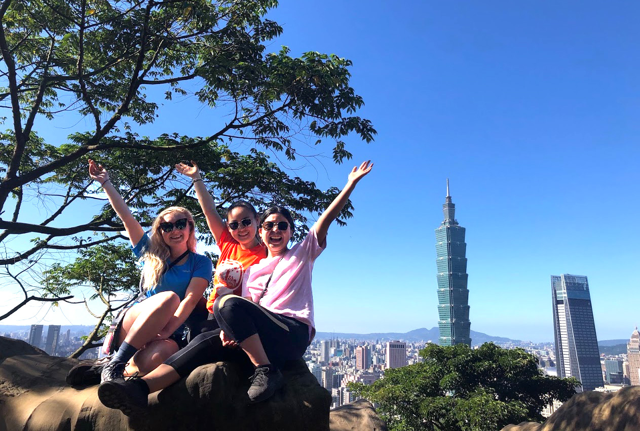 Anna French and two friends sitting on a rock with the Taipei skyline behind them