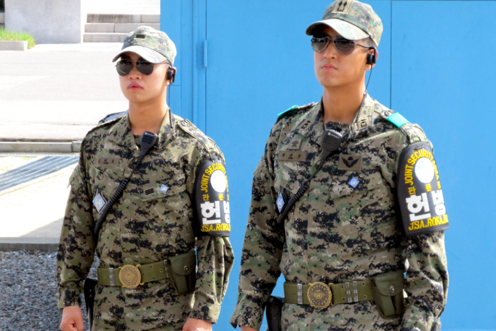 Two NK soldiers standing in full uniform with ear pieces in dmz