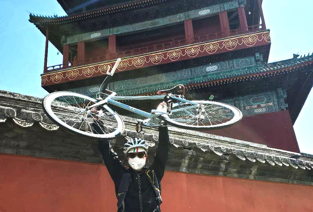 Duran holding a bike over his head in front of a traditional Chinese building