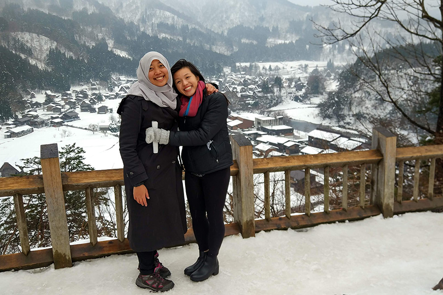 Charlene with her arm around a friend with a snowy village in the background