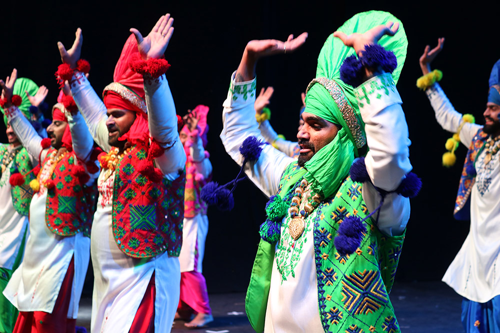 Bhangra dancers on stage dressed in brightly-coloured traditional dress