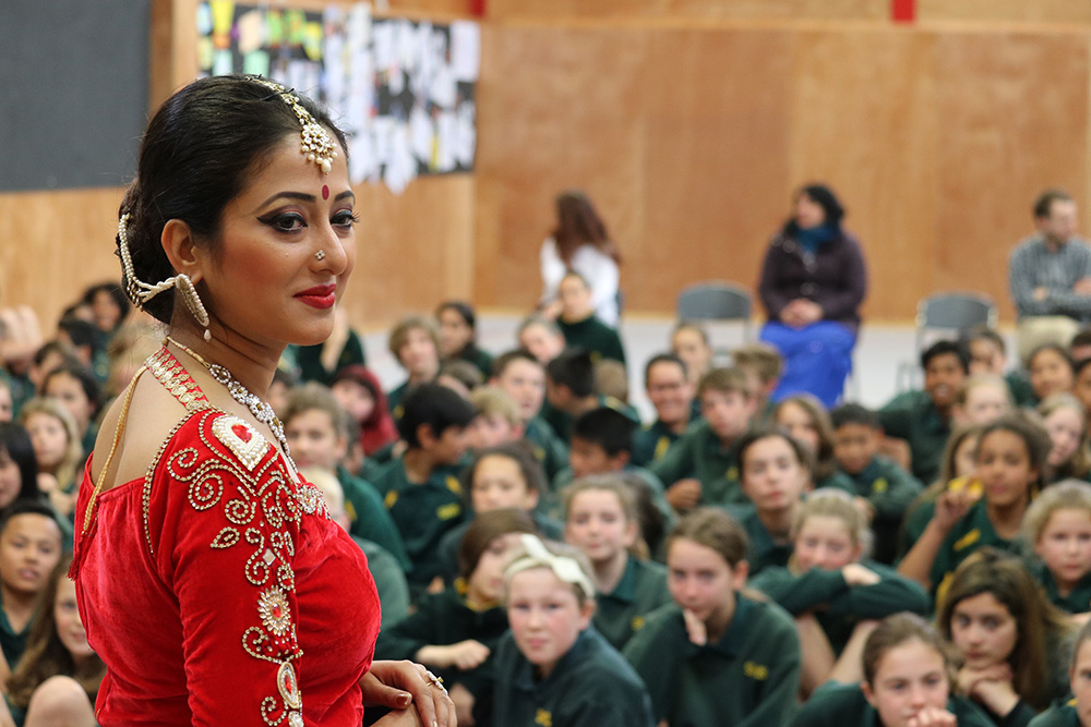 An Indian dancer in traditional attire standing in front of a hall of New Zealand school students