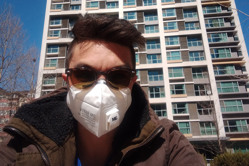 Duran Moy standing in front of an apartment building wearing a mask