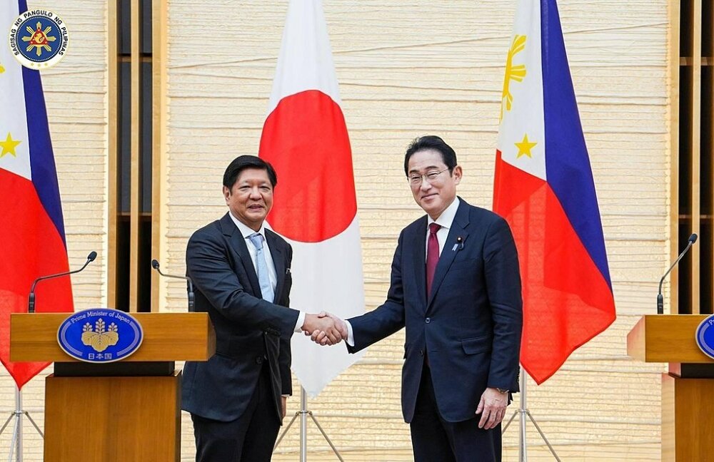 Japanese prime minister Fumio Kishida shaking hands with Philippine president Bongbong Marcos in front of the two nation's flags