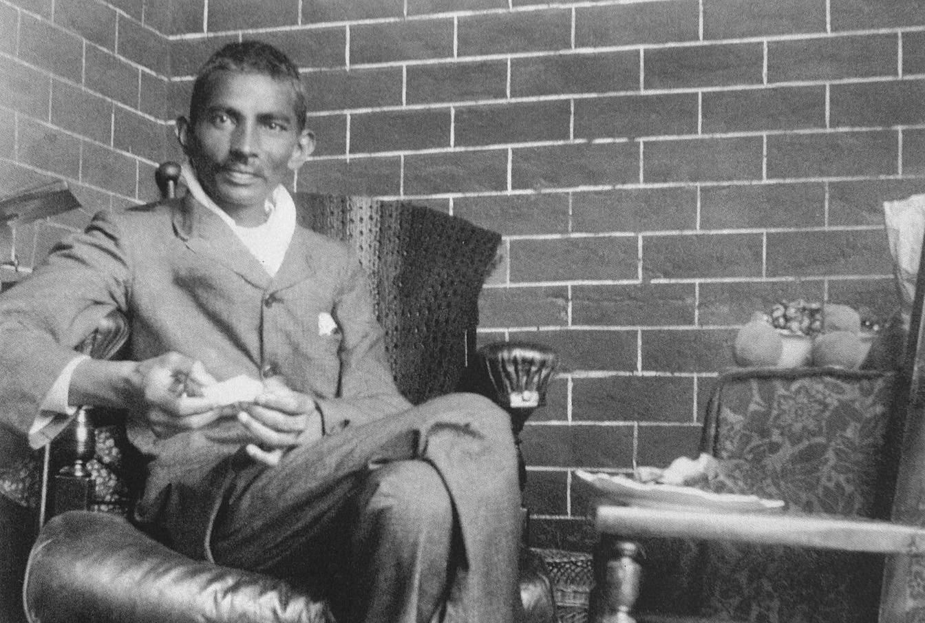 Gandhi as a young man sitting in a chair