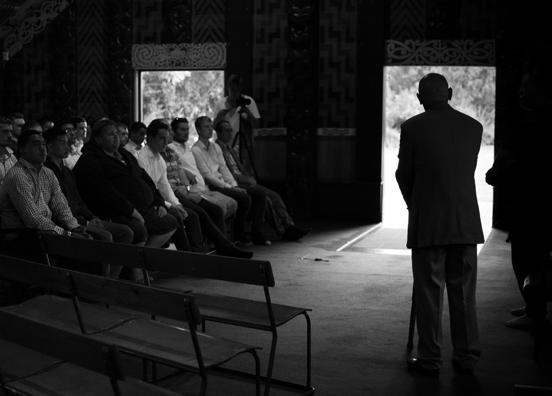 Black and white pic of man standing and speaking in front of seated group