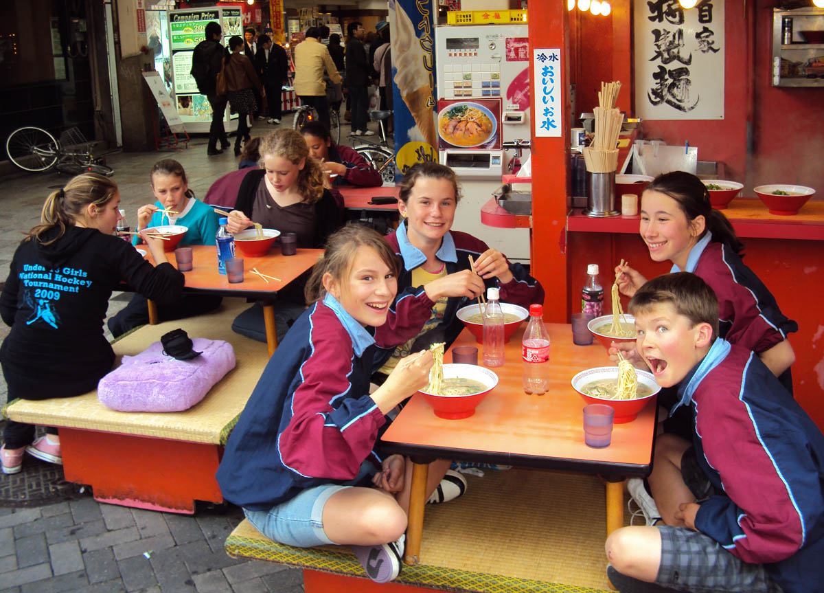 Students sitting at a low table using chopsticks to eat