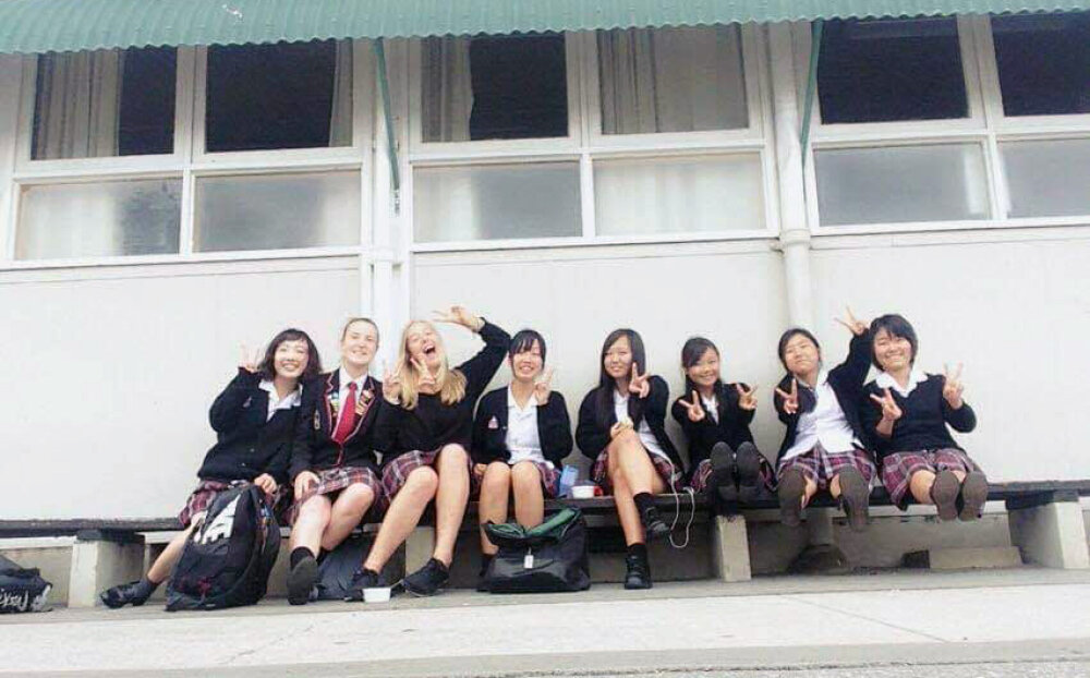 Megan sitting on school benches outside a classroom along with Japanese exchange students at her school
