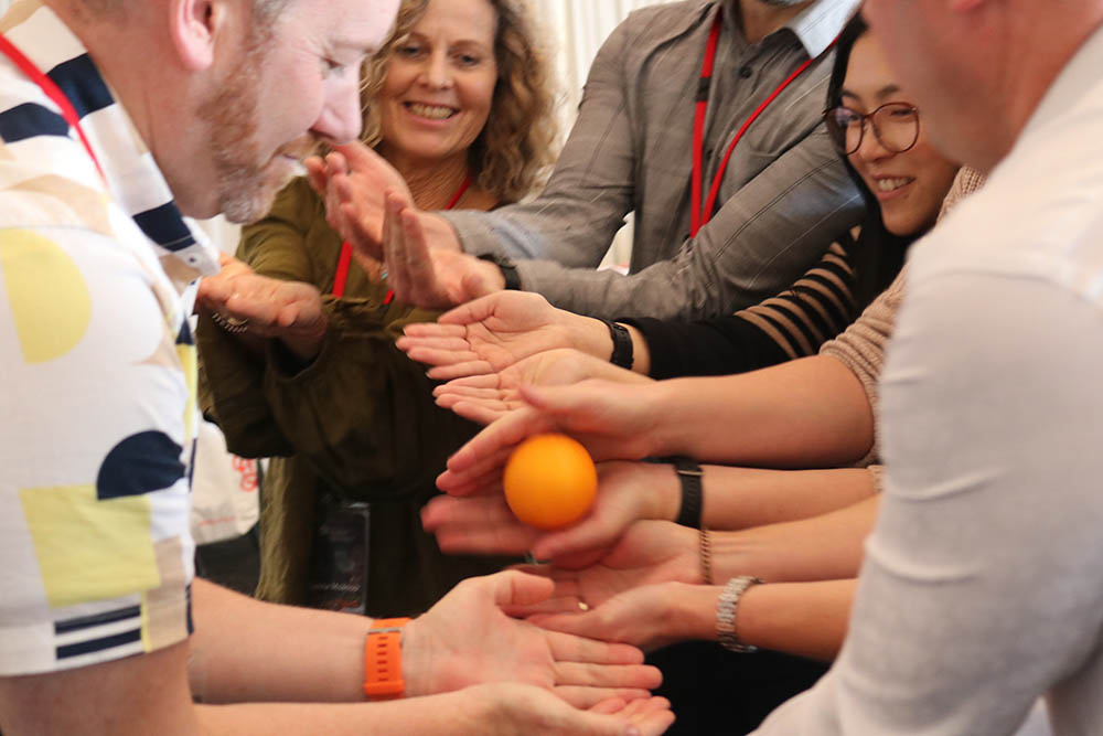 A group of teachers passing an orange from hand to hand as part of a warm-up game 