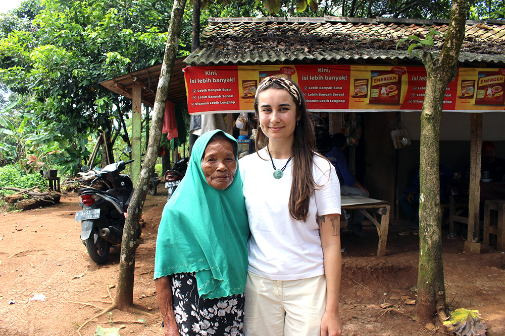 Isabella standing outside a small shop with a woman in a rural area of Indonesia