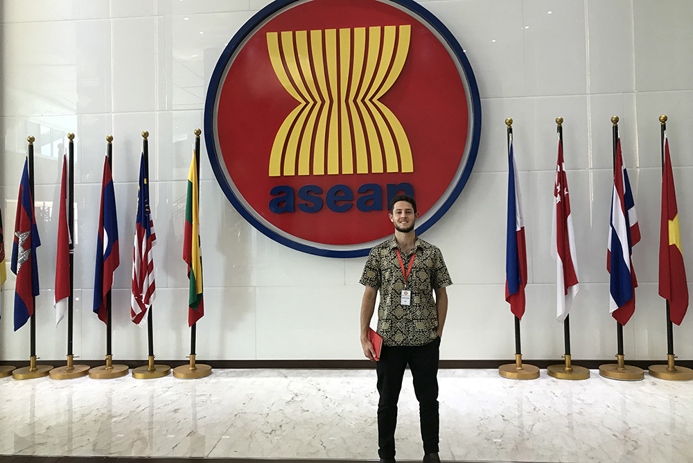 Jackson Calder standing in front of a large ASEAN logo and ASEAN nation flags