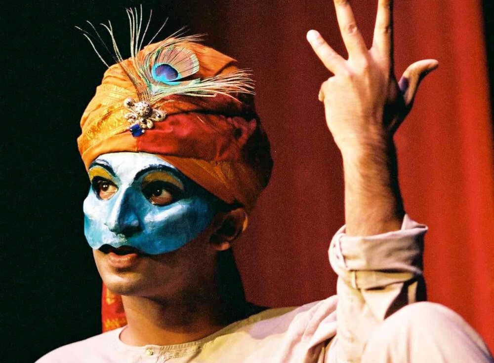 Jacob wearing a blue mask and orange headdress with a peacock's feather in it