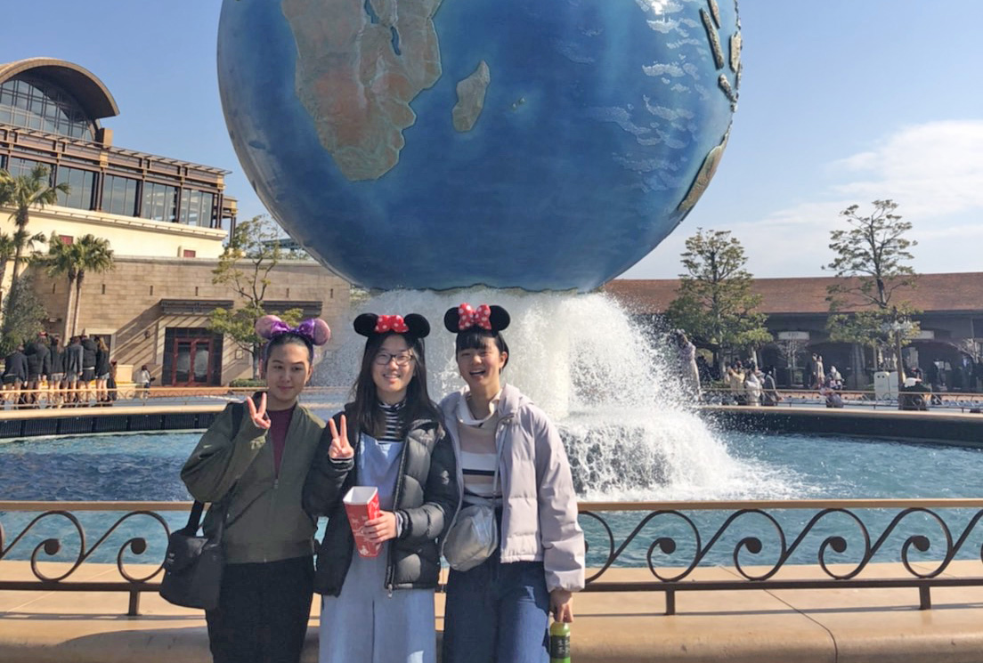 Varenica with two friends wearing mini-mouse hats in front of a fountain with a giant world globe on it