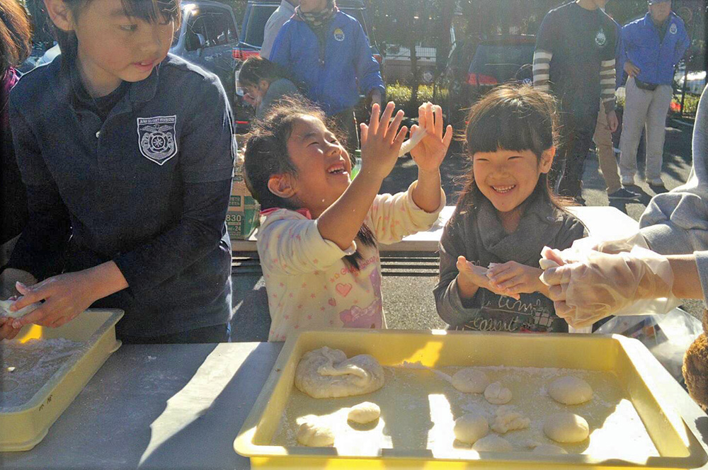 Two kids laughing while rolling dough to make mochi