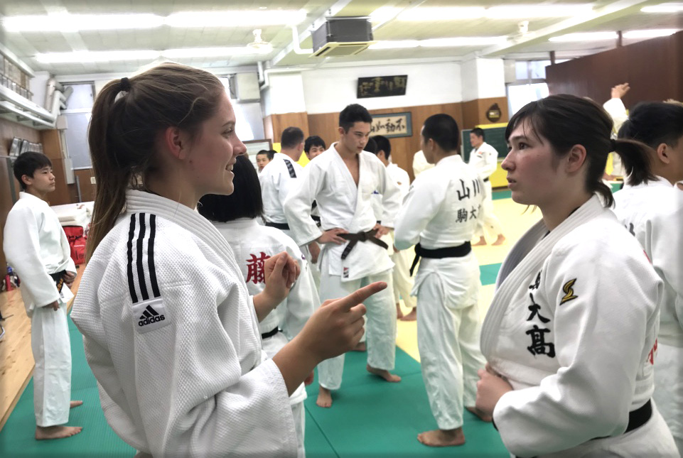 Two girls dressed in Judo robes chatting in a dojo