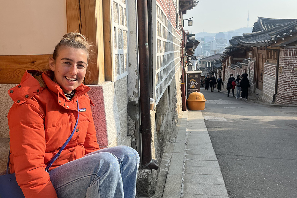 Libby sitting in the doorway with a street of traditional Korean houses and the skyline of Seoul in the background
