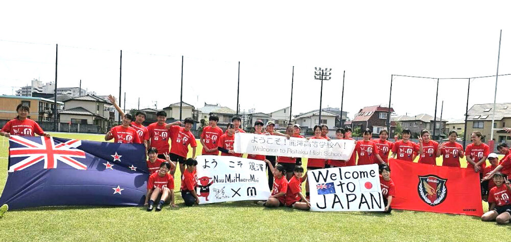 Japanese rugby players holding the New Zealand flags and welcome signs pose for a group photo on a field