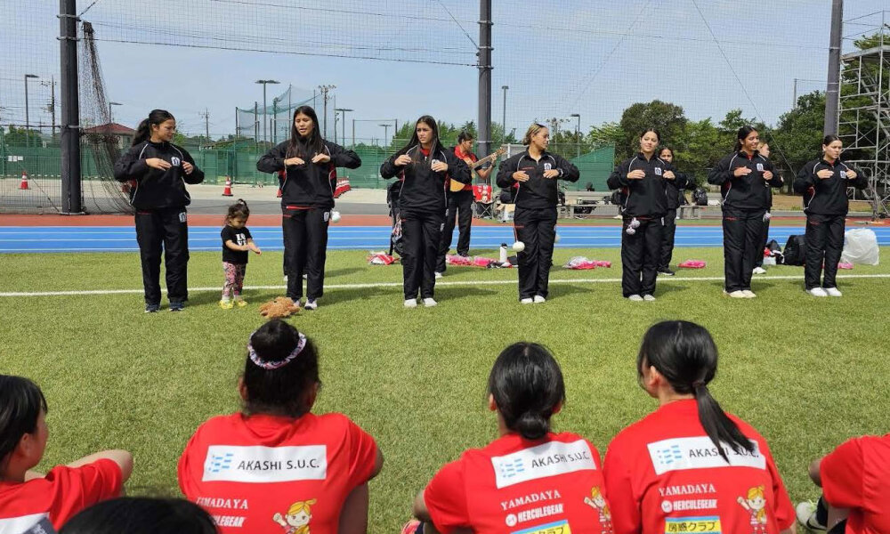 Manukura girls seven team performing a waiata on a field watched by a Japanese team