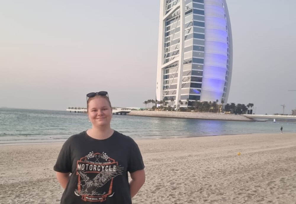 Hannah standing on a beach in Dubai with a high-rise building in the background