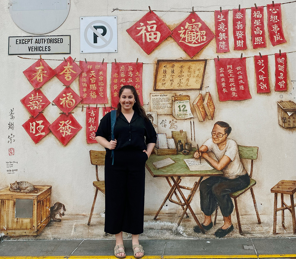 Melika standing in front of a mural of a man writing calligraphy