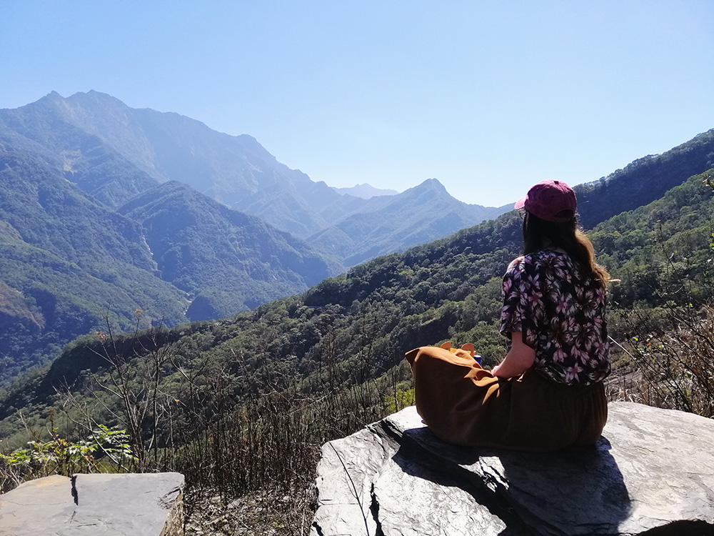 Monique sitting on a rock looking out over a range of forest-clad mountains