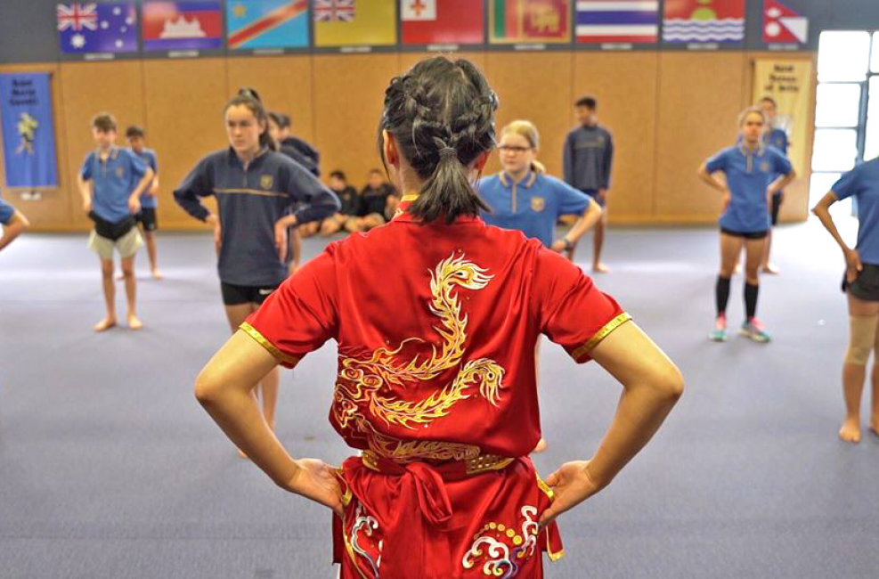 A wushu instructor standing in front of a class demonstrating a stance