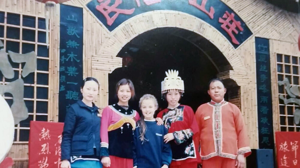 Nathalie Harrington as a child outside a school with four people dressed in traditional Chinese clothing