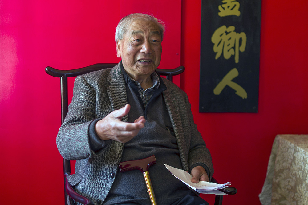 Dr James Ng sitting on a chair in a red room, gesticulating as he talks