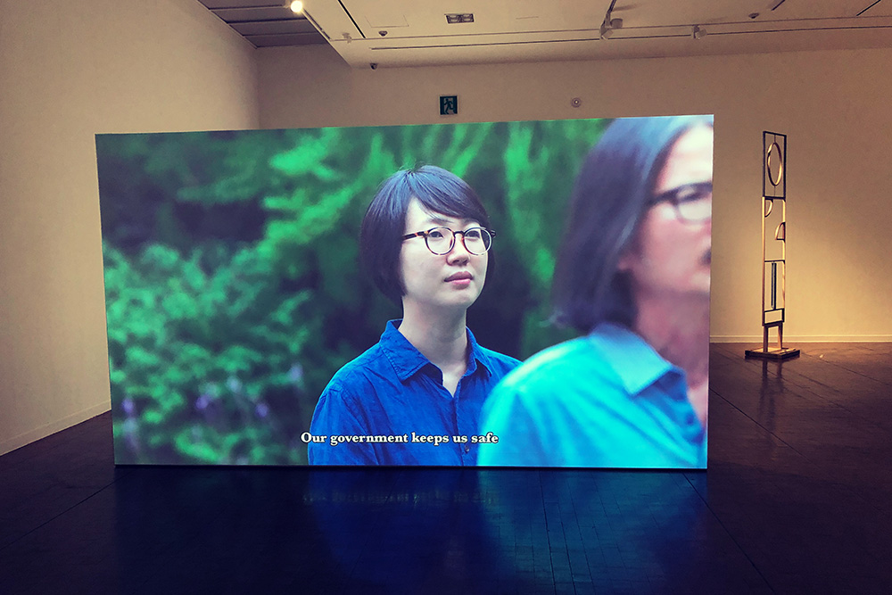 A gallery space with a video on a screen with a woman and the text